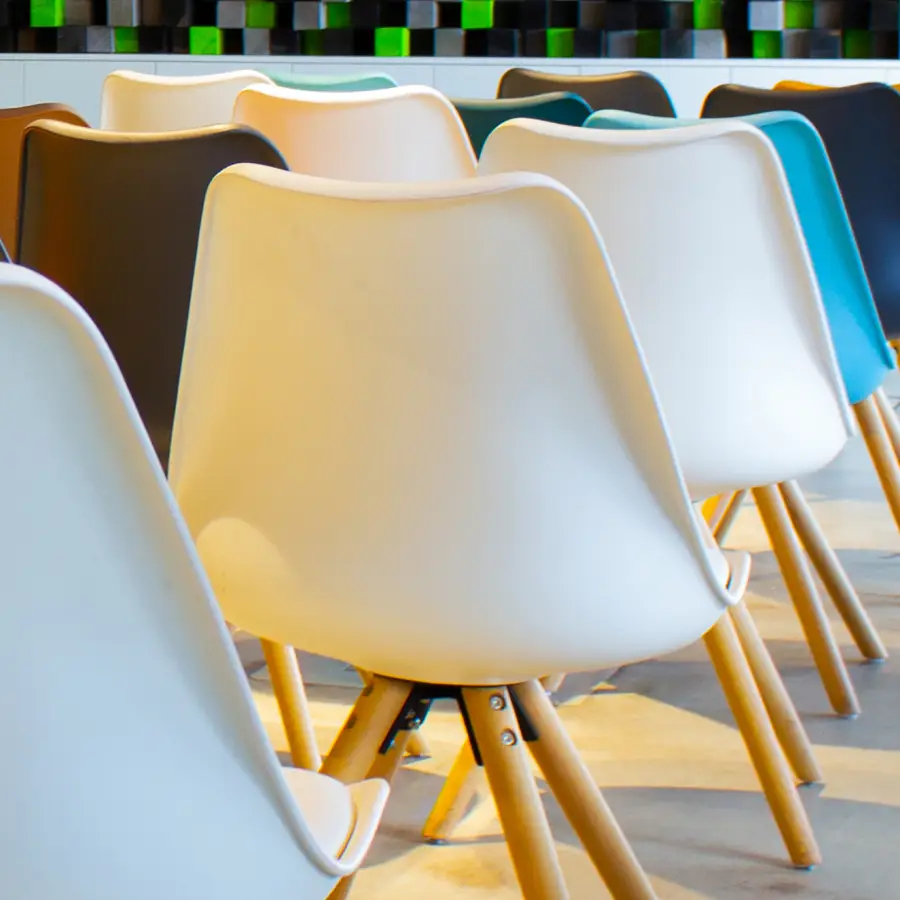 Die Stuhlreihen einer Seminarbestuhlung aus unterschiedlich farbigen Stühlen sind von hinten zu sehen.