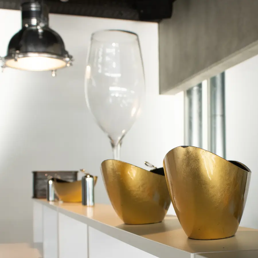 In der Küche stehen Designobjekte wie goldene Schalen, ein sehr großes Weinglas und eine Industrie-Lampe an der Decke.