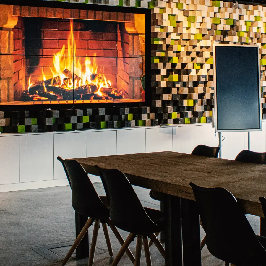 Ein Konferenztisch mit großem Display im Hintergrund, auf dem Kaminfeuer zu sehen ist, und ein digitales Whiteboard.