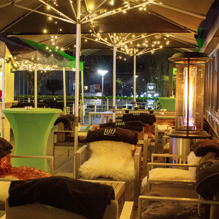 Eine Dachterrasse, die bei Nacht mit Sitzgelegenheiten, einer gemütlichen Lichterkette und Heizstrahlern ausgestattet ist.