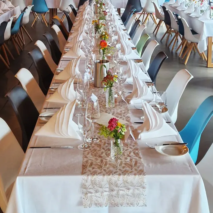 Ein langer Tisch, festlich und elegant gedeckt in Weiß, mit einer Tischdecke, weißen Servietten und Rosen.